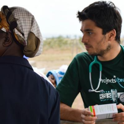 Male medical intern holds a box of medicine outside at a medical outreach during his Medicine internship in Kenya. Projects Abroad male intern waits to examine patients at a medical outreach in Kenya.